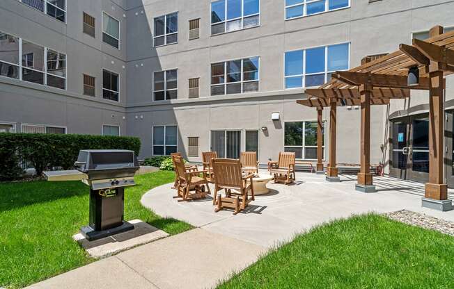 an outdoor patio with a grill and chairs in front of an apartment building