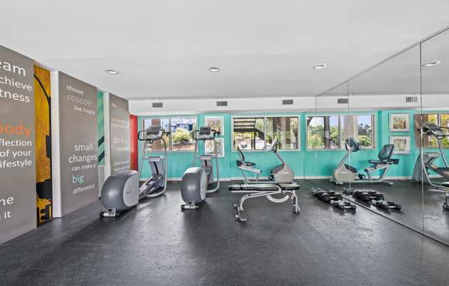 a gym with exercise machines and chairs in a large room with windows