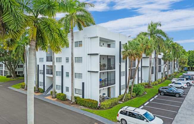 A white apartment building with a parking lot in front of it.