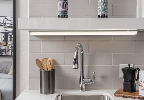 a kitchen sink with white countertops and a white shelf above it with two bottles of beer