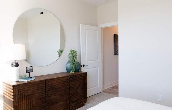 A bedroom with a round mirror above a wooden dresser.