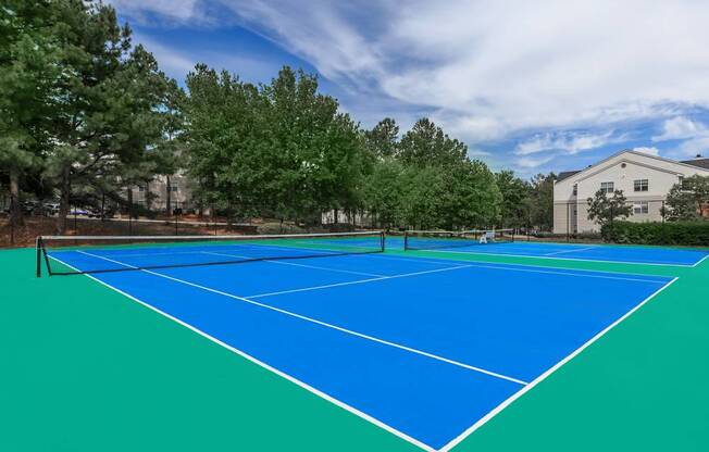 A blue tennis court surrounded by trees and a building.