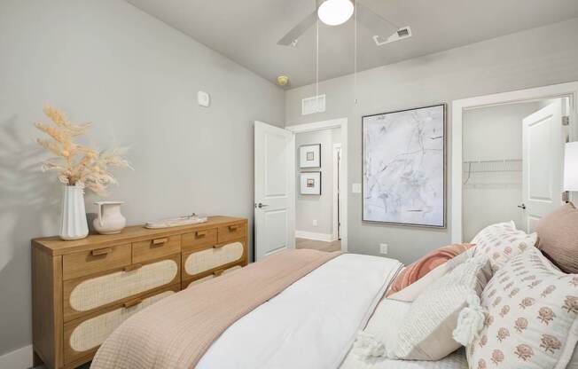 A bedroom with a bed, dresser, and a painting on the wall at The Ashton at East Park Apartments, Kennesaw