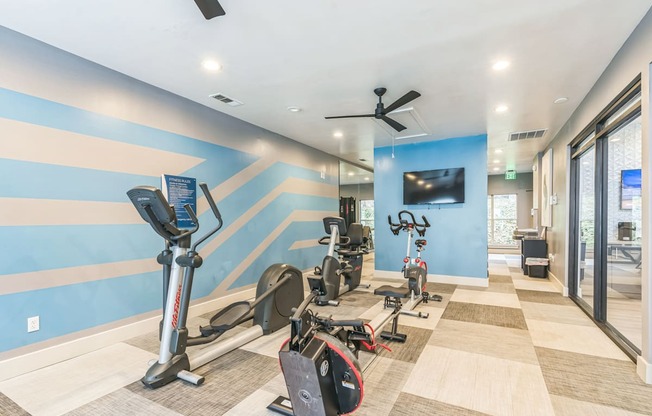 A gym with exercise equipment and a television on the wall.