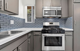 Blue tiled kitchen with stainless steel fridge, oven, and microwave.