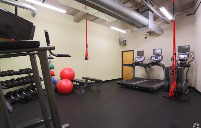 A gym with a red pull up bar, a bench, a treadmill, a weight rack and a rowing machine.
