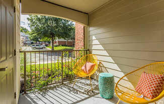 A yellow chair with a red and white pillow is on a porch.