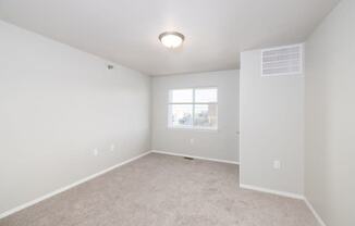 A spacious, empty room with a window and carpeted floor.