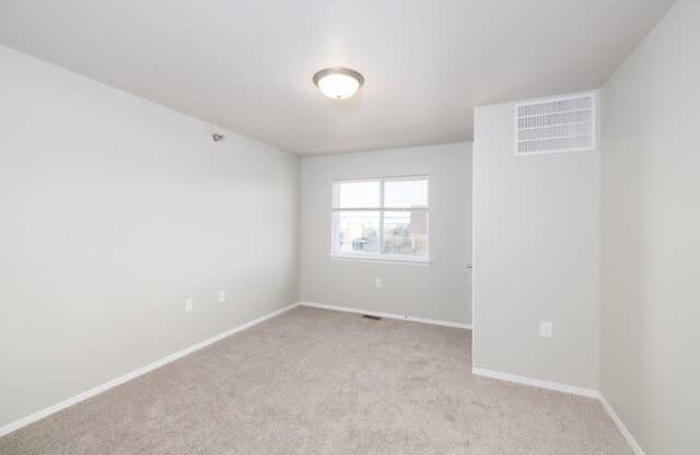 A spacious, empty room with a window and carpeted floor.