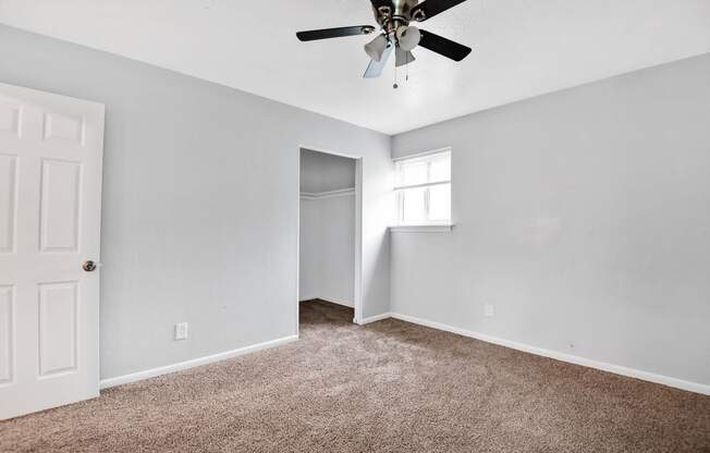 large carpeted room with ceiling fan, window, and closet