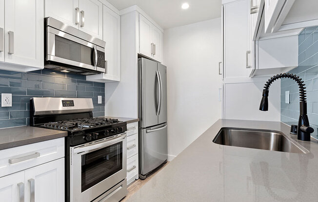 Blue tiled kitchen with quartz stone counters and stainless steel microwave, oven, fridge, and fixtures.