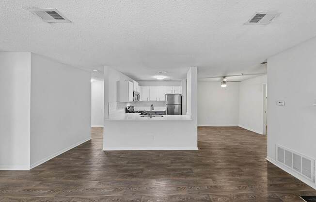 A kitchen with a sink and a refrigerator is visible through a window in a white room.