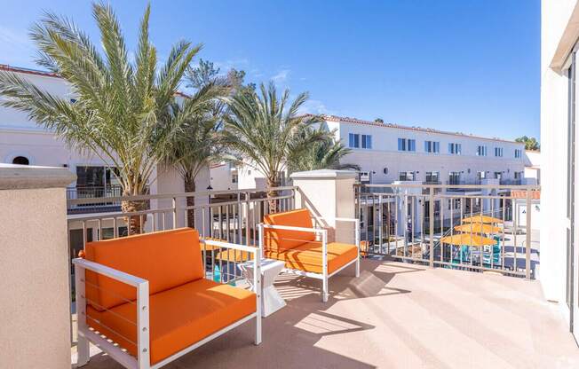 Two orange chairs are on a patio with a palm tree.