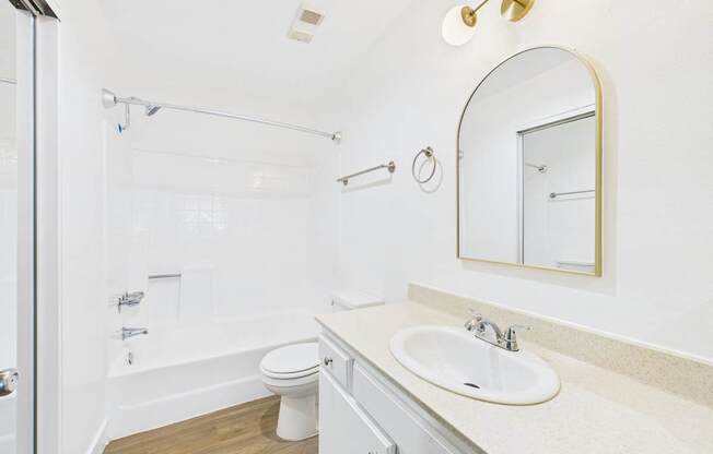 A white bathroom with a sink, mirror, and toilet.