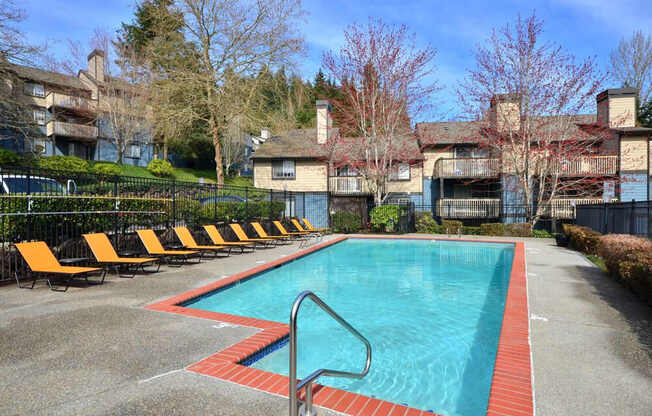 A swimming pool surrounded by orange lounge chairs and apartment buildings.