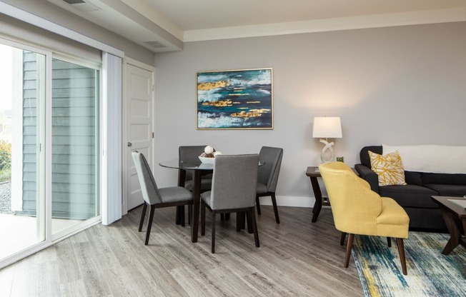 A modern living room with a grey sofa, a grey dining table and a yellow chair.