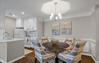 Bright and contemporary kitchen and dining space featuring white cabinetry, updated appliances, wood style flooring, and elegant lighting at Kelly’s Ridge Apartments in Columbia, Missouri.