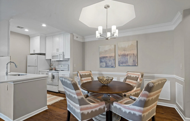 Bright and contemporary kitchen and dining space featuring white cabinetry, updated appliances, wood style flooring, and elegant lighting at Kelly’s Ridge Apartments in Columbia, Missouri.