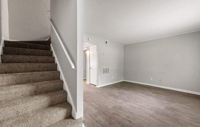 the living room and entryway of a renovated house with carpeted stairs