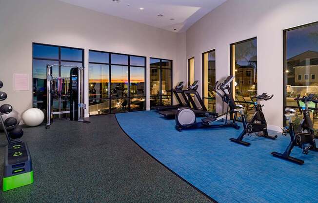 A gym with a view of the sunset through the windows.