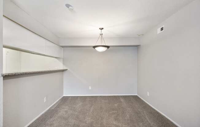 an empty room with carpet and a light hanging from the ceiling