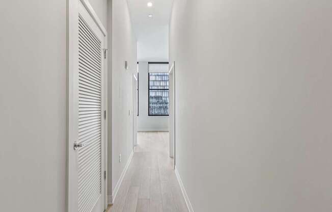 A long white hallway with a door on the left and a window with bars on the right.