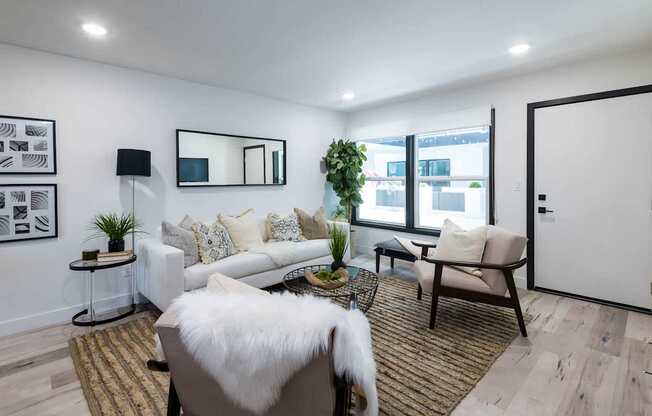 A modern living room with a white couch, a black and white mirror, a white fur throw, and a brown rug.