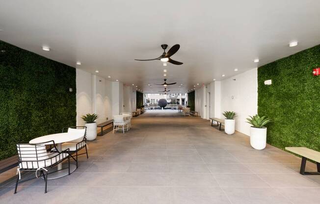 a long corridor with benches and plants and a ceiling fan
