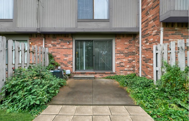 A brick building with a grey door and a concrete walkway leading to it.
