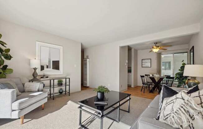 A living room with a grey couch, a black coffee table, and a dining area in the background.