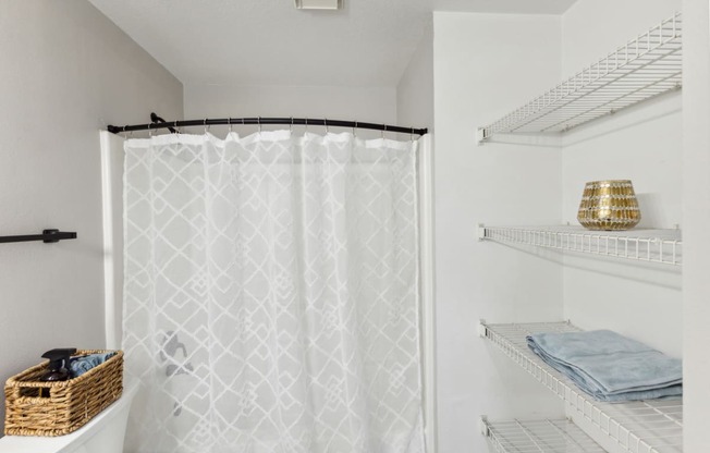 a shower with a white shower curtain and shelves with towels