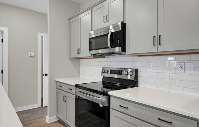 an empty kitchen with white cabinets and a stove and microwave