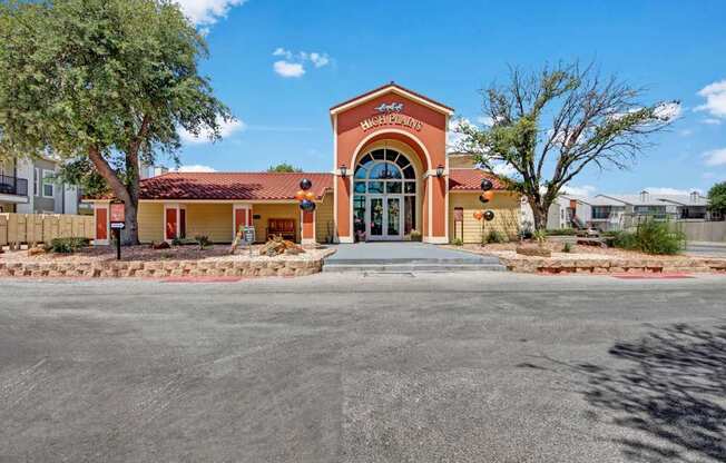 A welcoming leasing office exterior here at High Plains with a charming entryway, arched glass doors, and warm-toned stucco accents. Desert landscaping, mature trees, and a tiled roof create a polished and inviting first impression for residents and guests.