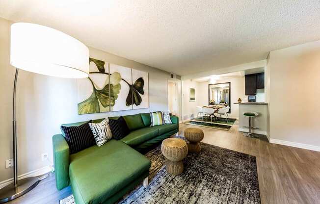 Living room with modern lighting and big green couch with  dining room and breakfast bar in background