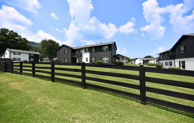 a black fence in front of a green field with houses in the background