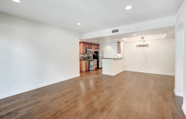 an empty living room and kitchen with wood flooring and a chandelier