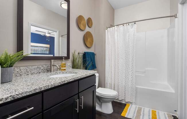 A bathroom with a white toilet, a sink with a granite countertop, and a shower with a white curtain.