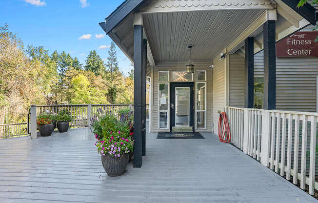 A fitness center entrance with a wooden deck and potted plants.