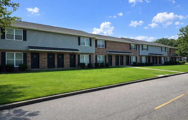 A row of houses with green lawns and trees in the background.