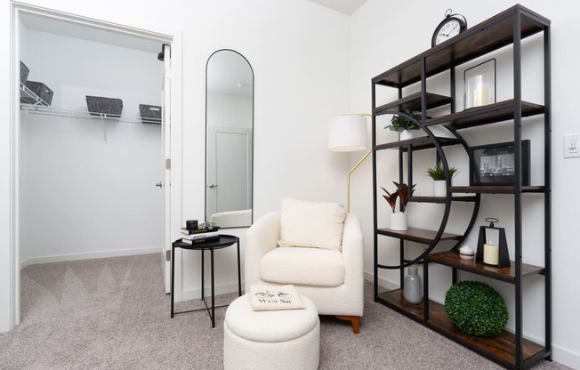 A white chair sits in front of a mirror in a room with a shelf.