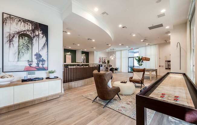 A billiard table is in the foreground of a well-lit room with a couch, chair, and a cabinet with a painting on it.