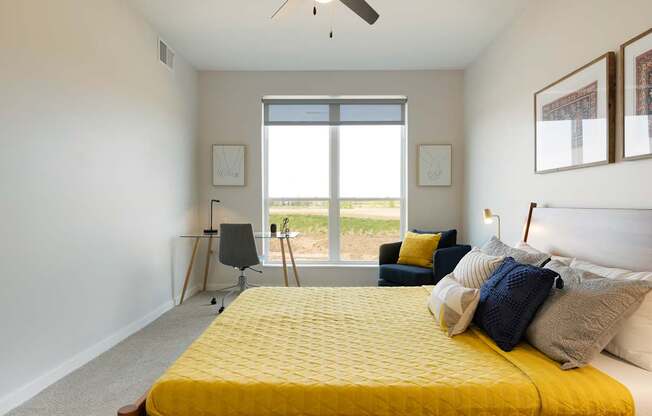 A bedroom with a yellow bed and a window overlooking the grass.