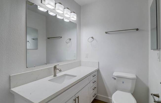 A white bathroom with a sink, toilet, and mirror.