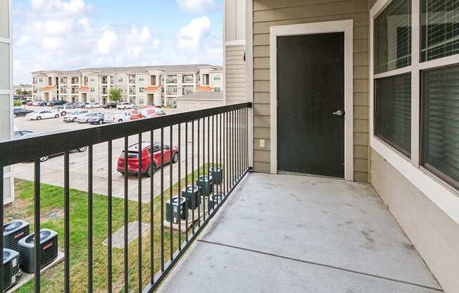 A balcony with a black railing and a red car parked in the parking lot.