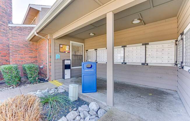 A blue recycling bin sits under a covered porch.
