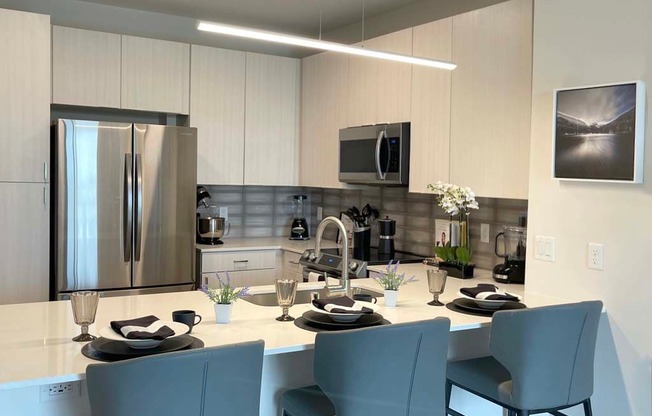 A modern kitchen with a white countertop and grey chairs.