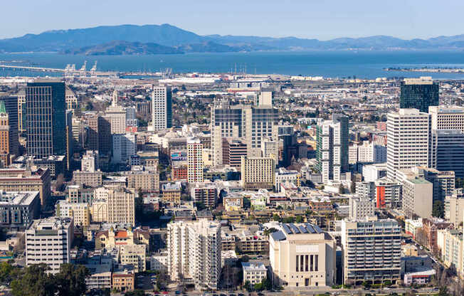 A cityscape with a mix of modern and older buildings, a bridge in the distance, and a mountain range in the far background.
