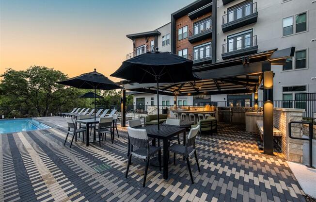Poolside chairs and tables with a covered barbecue grilling station near The Shiloh's 4-story apartment building.