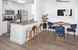 A modern kitchen with a white island, wooden chairs, and a ceiling fan.