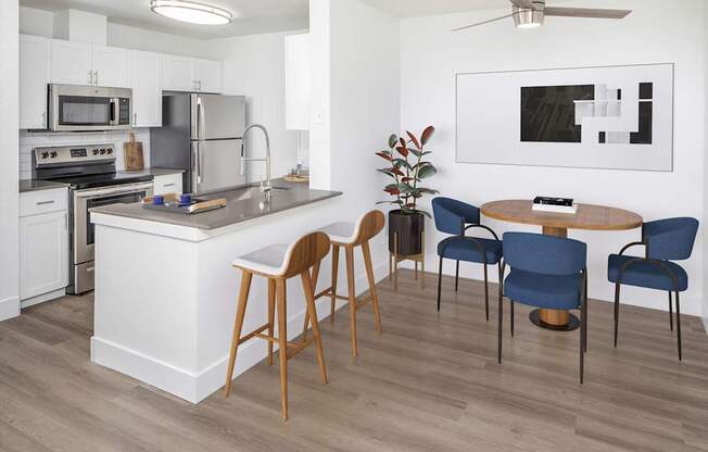 A modern kitchen with a white island, wooden chairs, and a ceiling fan.